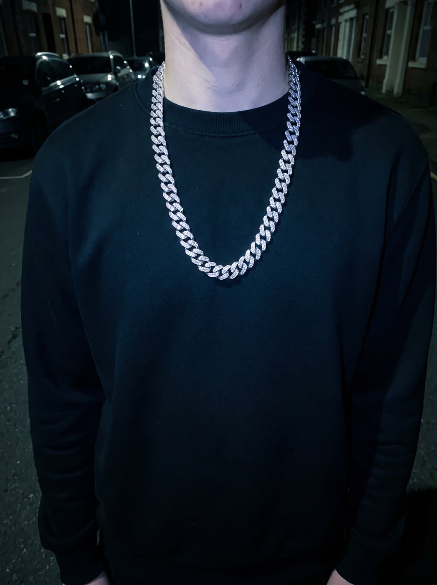 Iced cuban chain over a plain black hoodie, shot with direct flash