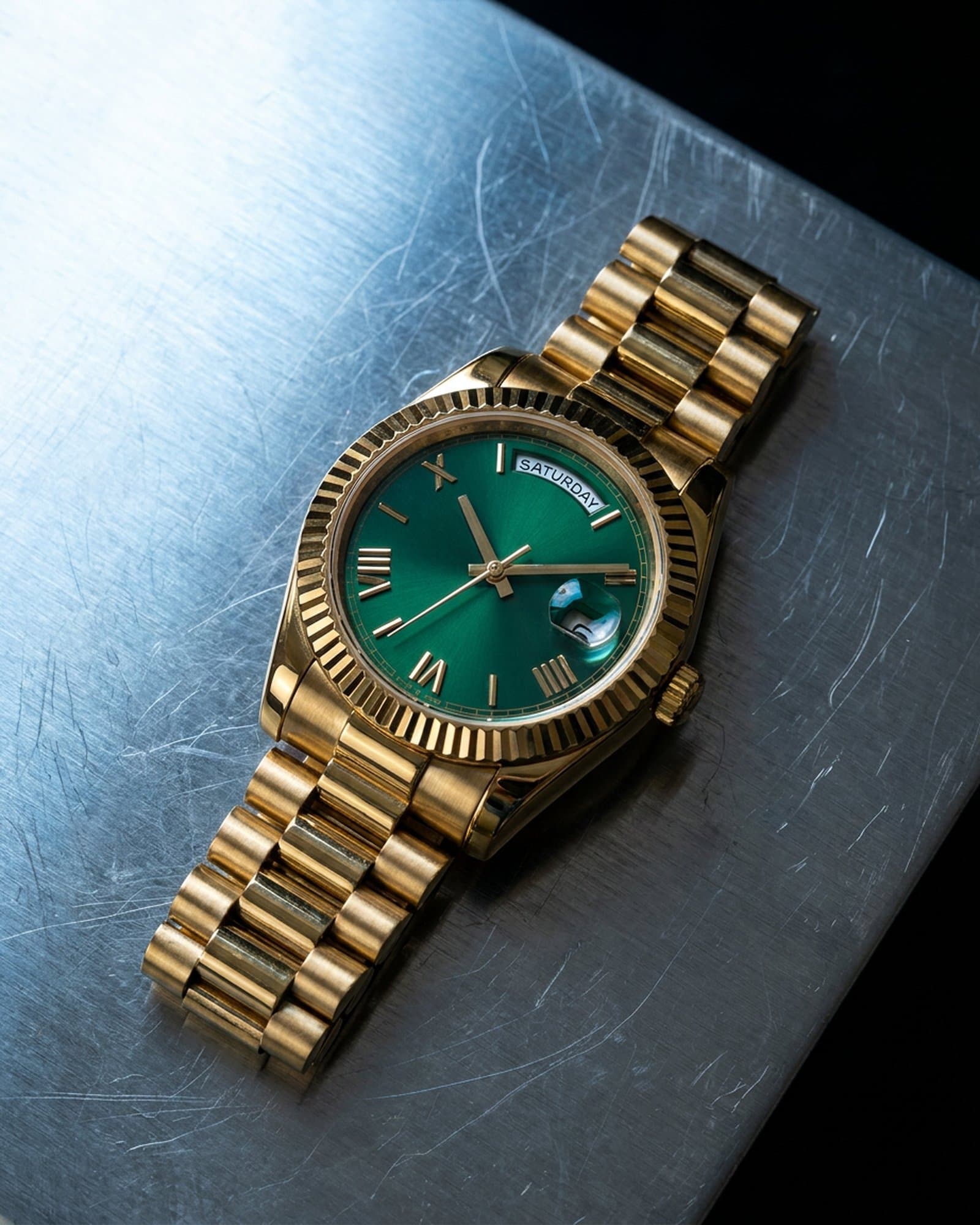 Gold watch with a green dial lying on scratched steel under a cold light