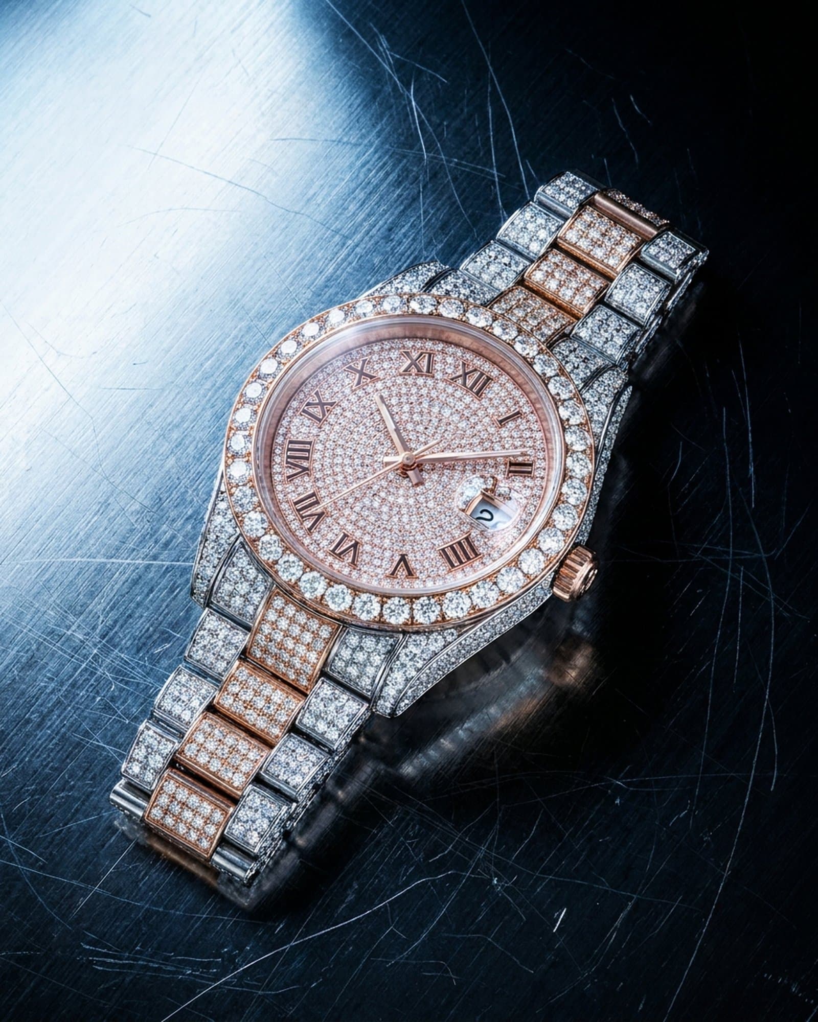 Iced rose two-tone watch with a pink pave dial lying on scratched steel