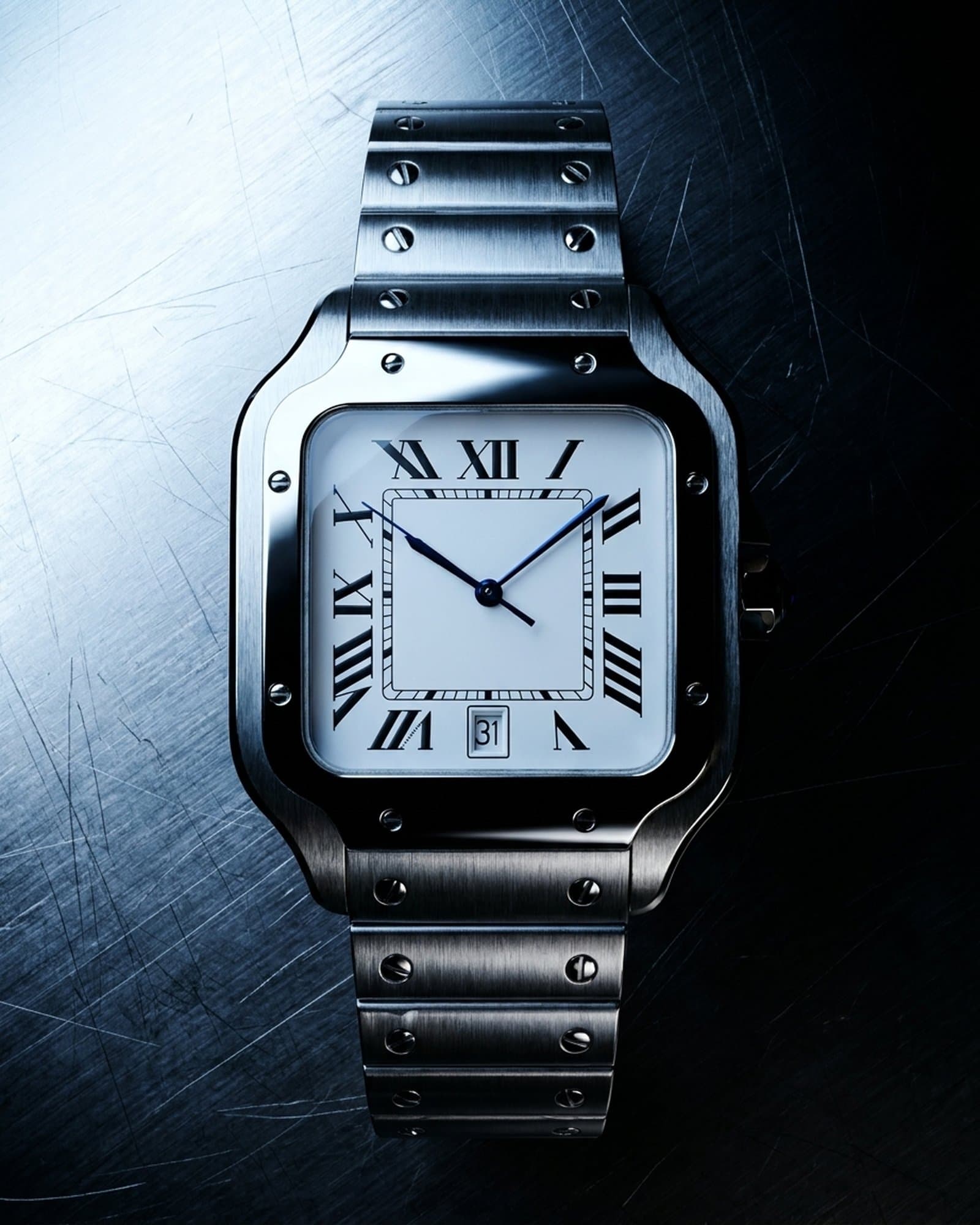 Square watch with a white dial lying on scratched steel under a cold light