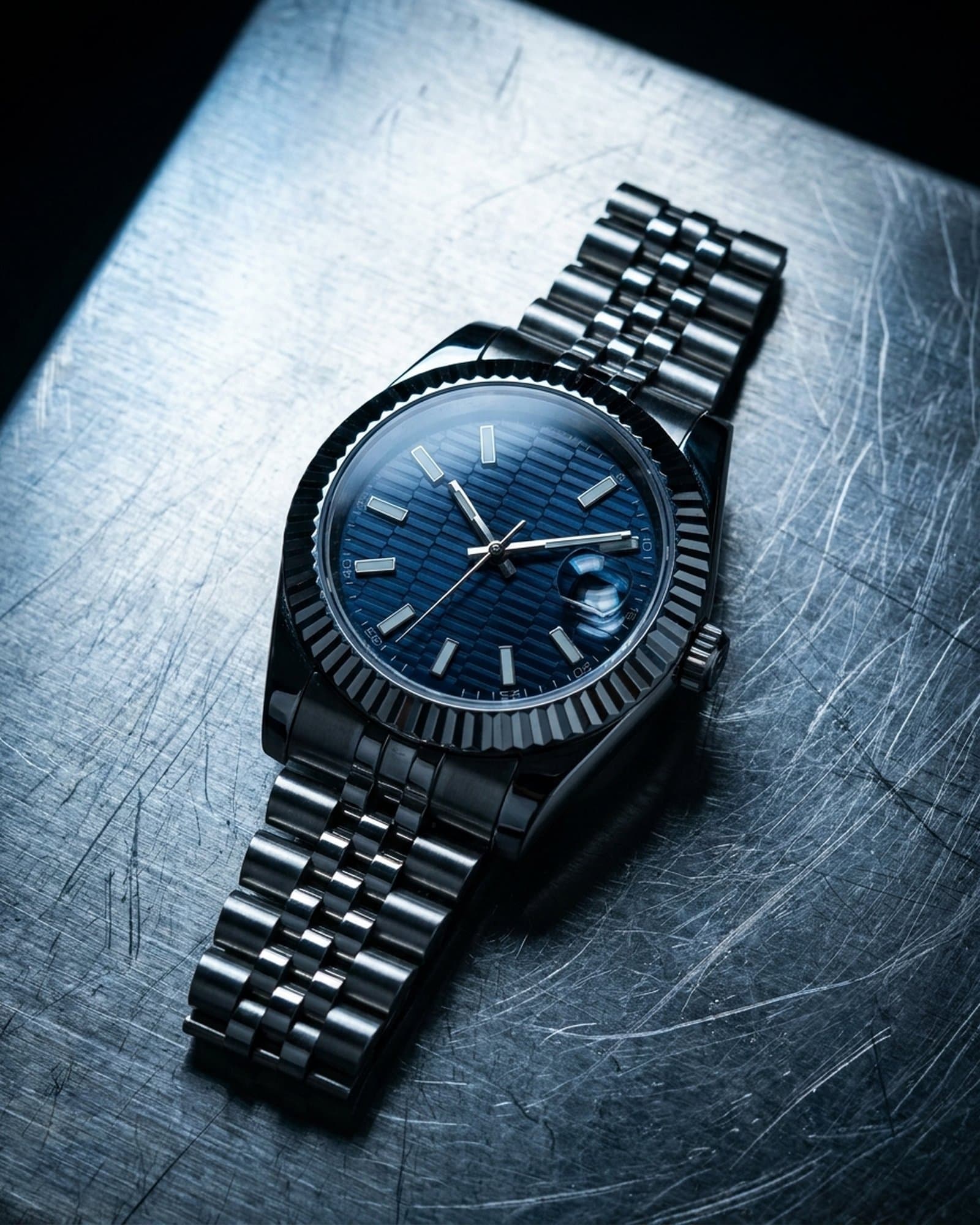 Steel watch with a blue ridged dial lying on scratched steel under a cold light