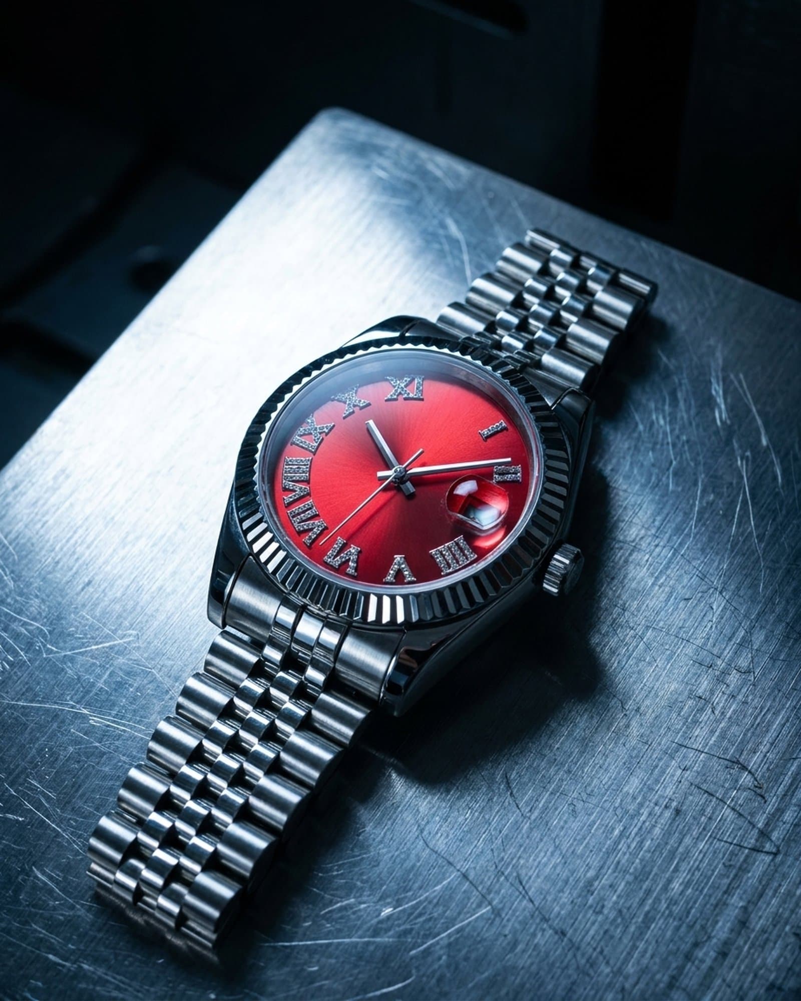 Steel watch with a red dial lying on scratched steel under a cold light